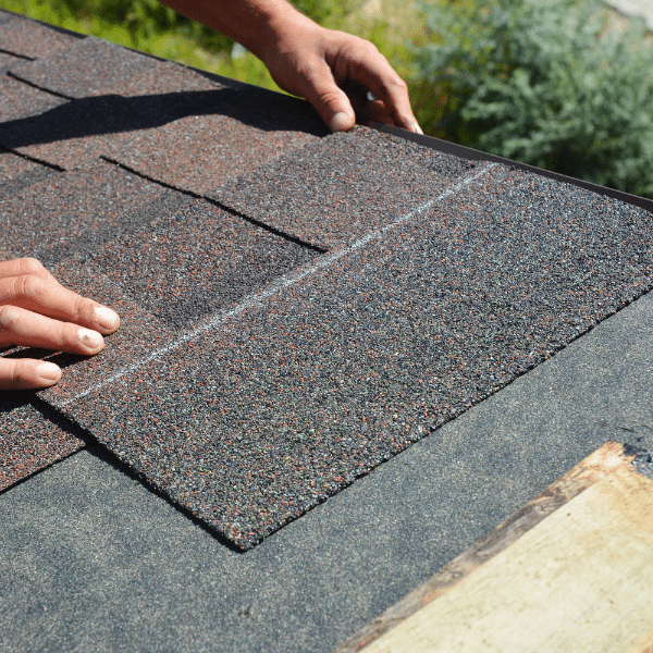 A person installing asphalt shingles on a roof, expertly aligning the shingles by hand as part of professional Roofing Services in Millcreek UT.