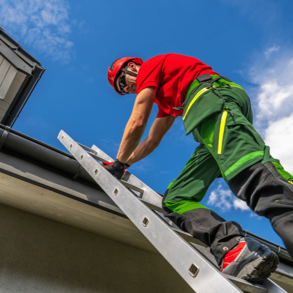 Wearing safety gear, a person climbs a ladder to work on the roof of a building in Salt Lake City, possibly performing an emergency roof leak repair under a partly cloudy sky.