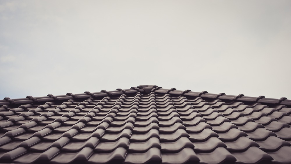Close-up view of a dark, wavy-tiled roof taken from below in Holladay, Utah, with the roof’s peak centered and a cloudy sky in the background—an excellent example of quality roofing services in the area.