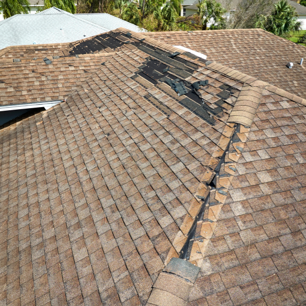 A house roof with brown shingles shows significant damage and missing shingles along the ridge and upper sections, suggesting it's time to consider roofing cost or even the new roof cost Utah homeowners might face.