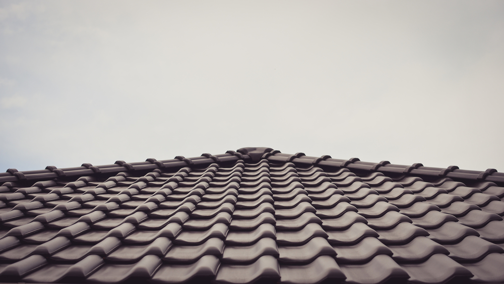 A close-up view of a dark-colored tiled roof, photographed from below with a cloudy sky in the background, highlighting quality roof installation often provided by professional roof services in Utah.