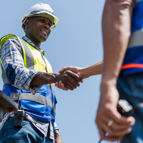 A construction worker in a safety vest and helmet shakes hands with another person outdoors under a clear blue sky, possibly discussing New Roof Cost Utah or other roofing cost details.